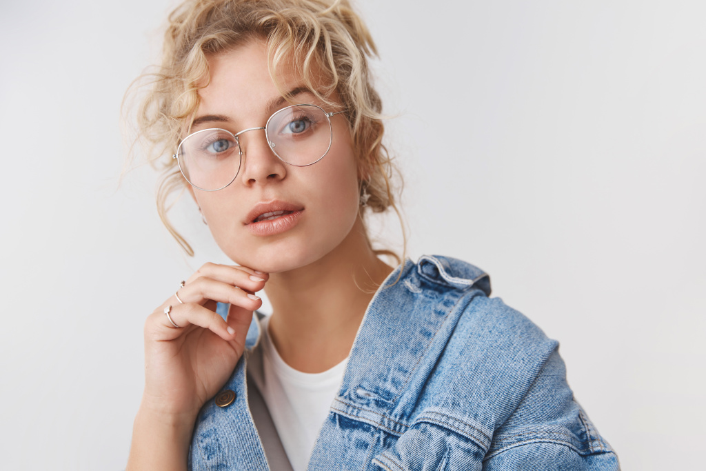 close-up-elegant-good-looking-fashionable-blond-blue-eyed-blogger-wear-transparent-glasses-denim-jacket-touching-chin-thoughtful-look-camera-intrigued-interested-standing-white-wall.jpg
